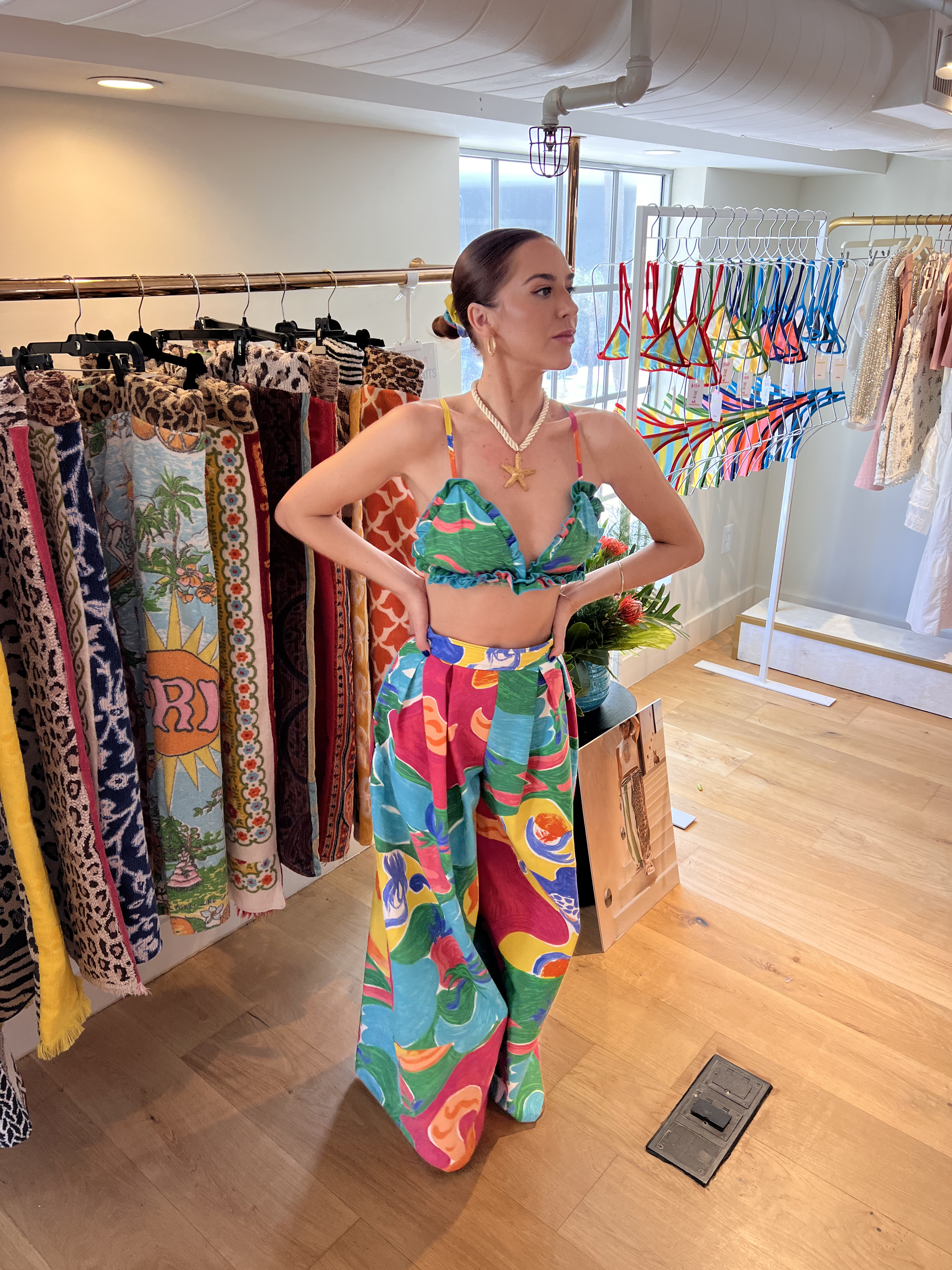 Woman in a colorful tropical outfit standing in a boutique with vibrant clothing displays.