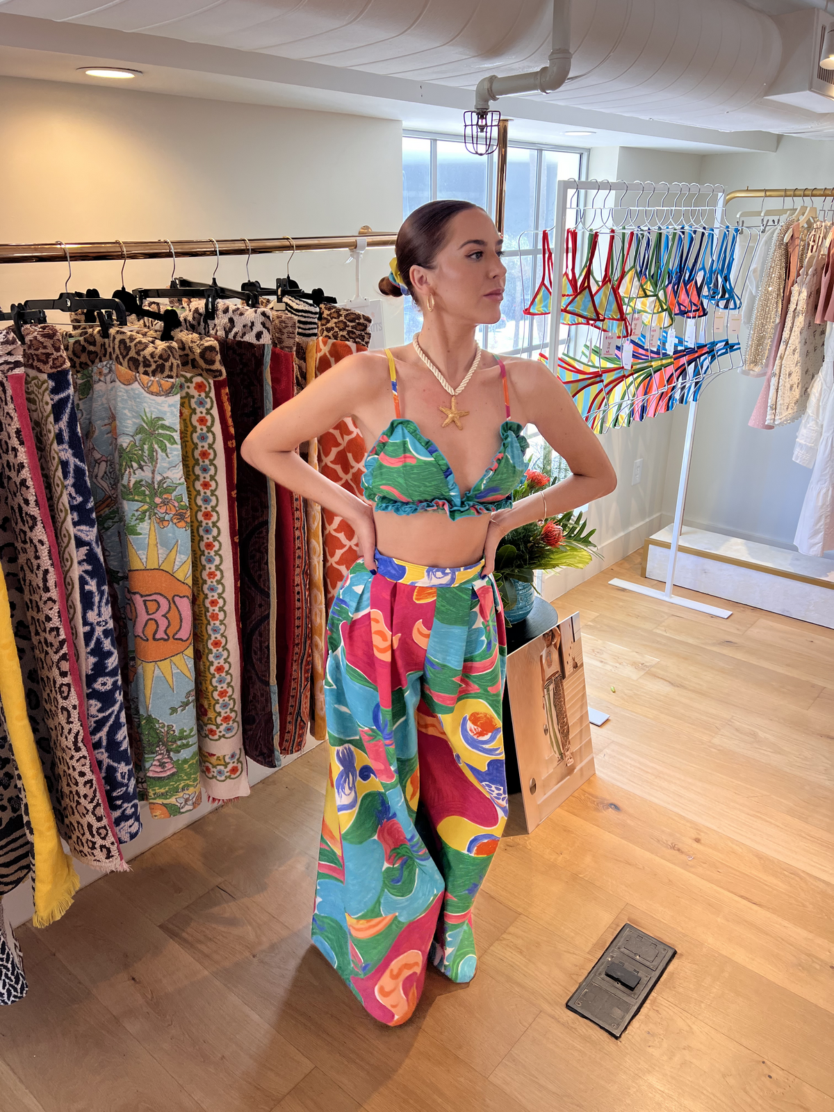 Woman in a colorful tropical outfit standing in a boutique with vibrant clothing displays.